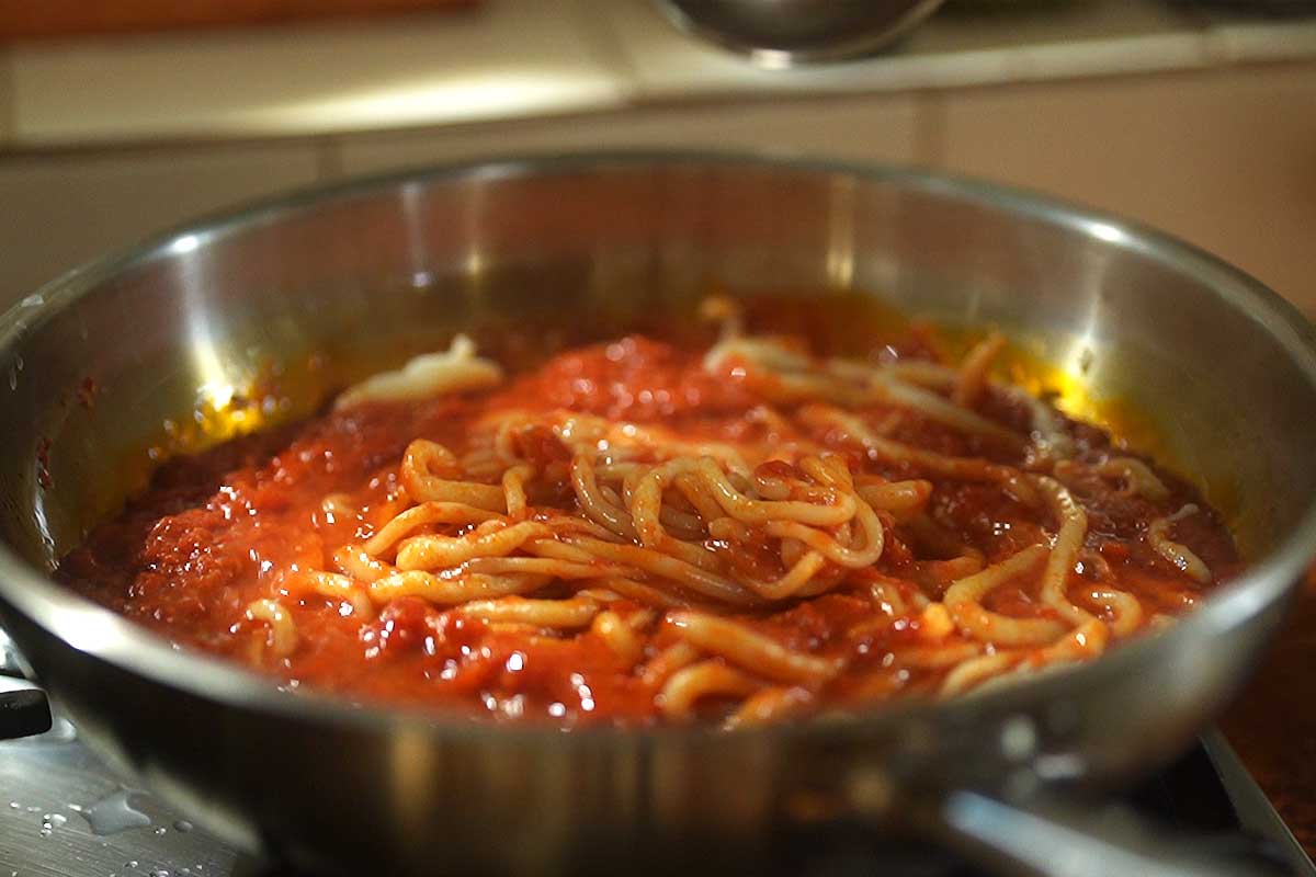 Pici being tossed in aglione sauce with pasta water until glossy and coated