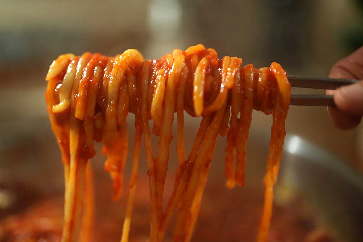 Close up of hand-rolled pici pasta coated in sweet garlic tomato sauce