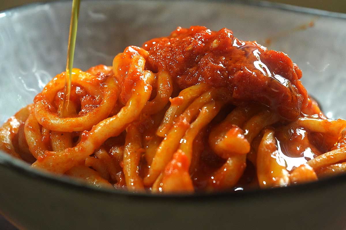 Pici all'Aglione served in bowl with olive oil drizzle and cracked black pepper