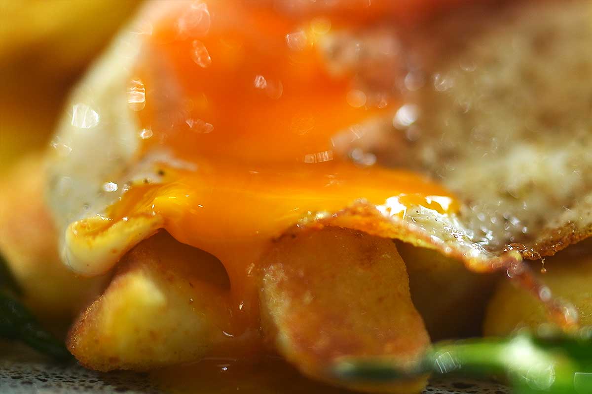 Close-up of runny egg yolk coating a fork full of crispy potato