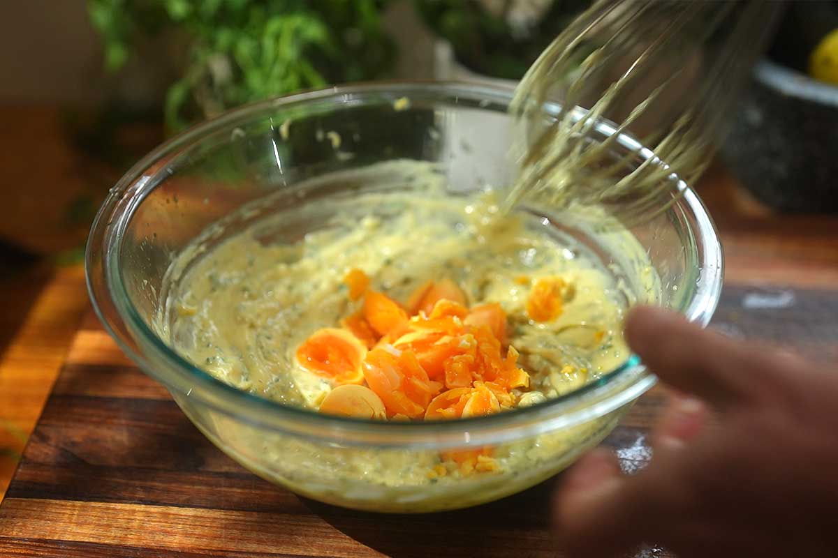 The mayonnaise being whisked, thick and glossy, with the cooked yolks folded through