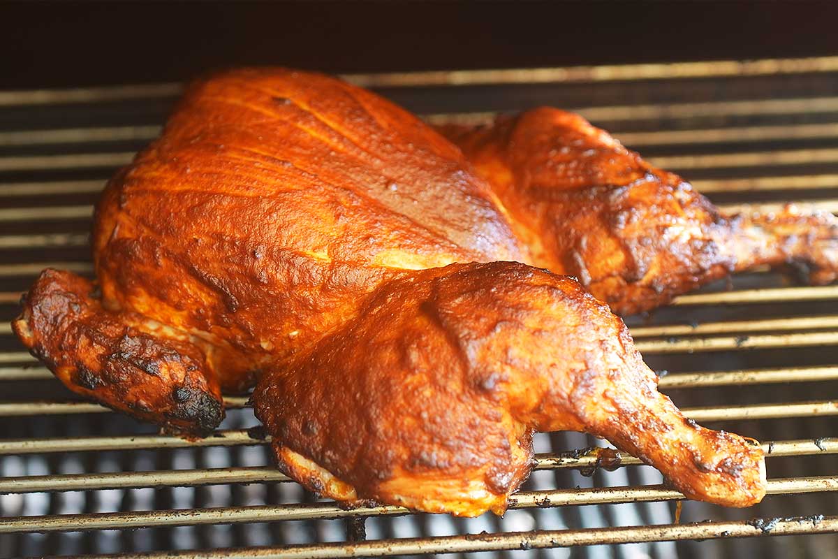 Whole spatchcocked chicken glistening with piri piri sauce, fresh off the charcoal grill