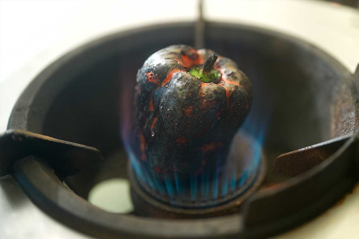 Whole red pepper blackened over open flame]