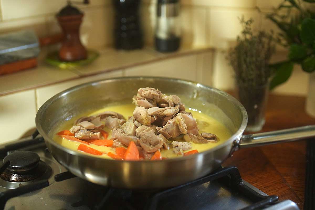 Close up of chicken and vegetables gently poaching in stock in a large pot