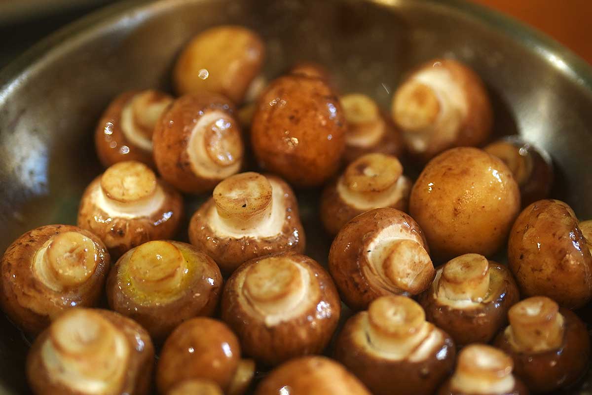whole mushrooms cooking gently in a frying pan with a small amount of liquid, no browning