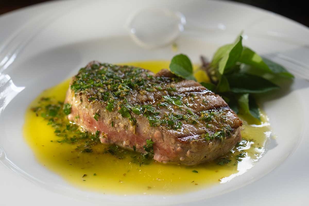 Overhead shot of the whole seared tuna steak sliced open, showing the dark crust and pink pink centre, sauce pooled around it