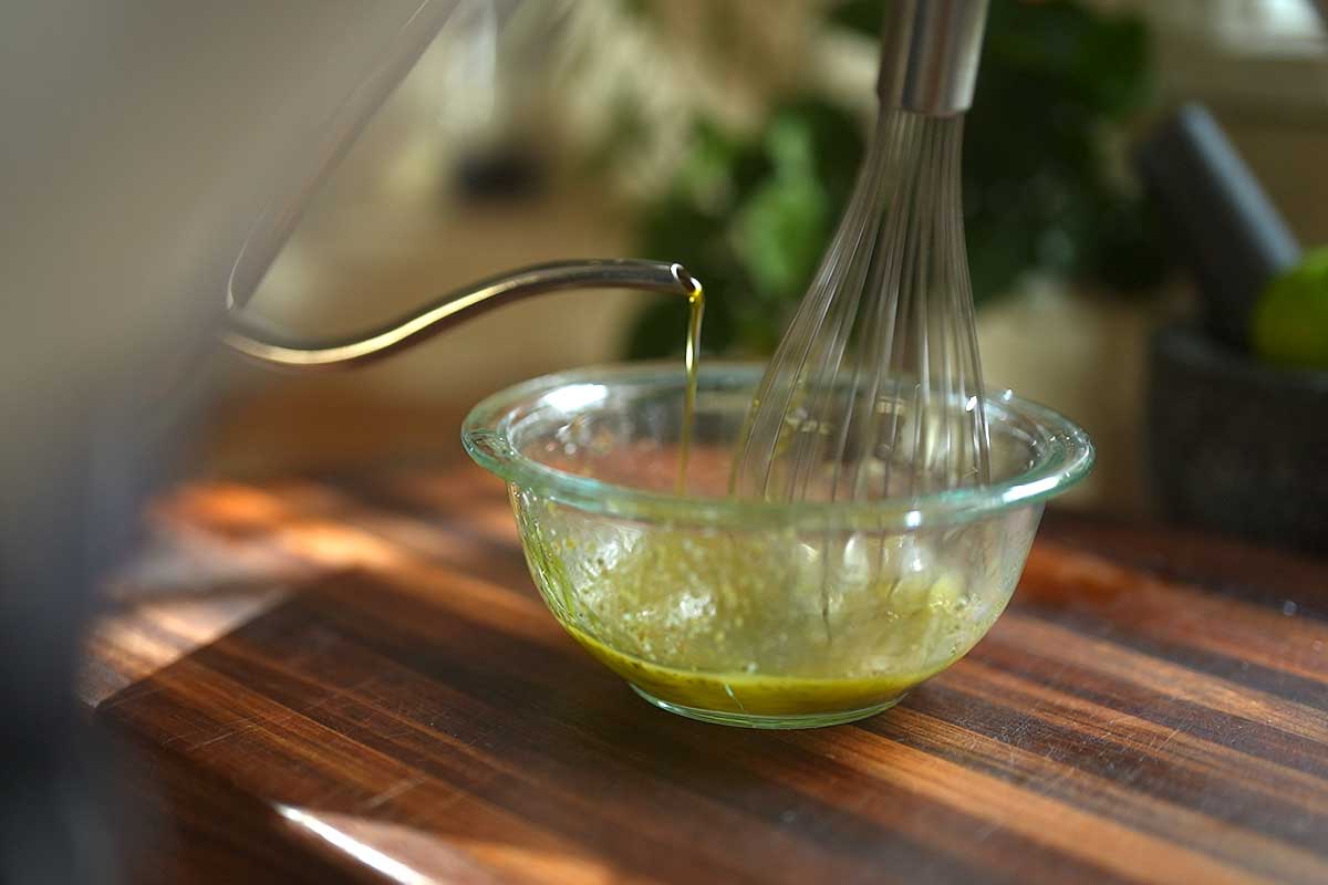 Close up of the salmoriglio being whisked in a bowl, showing the emulsion coming together]