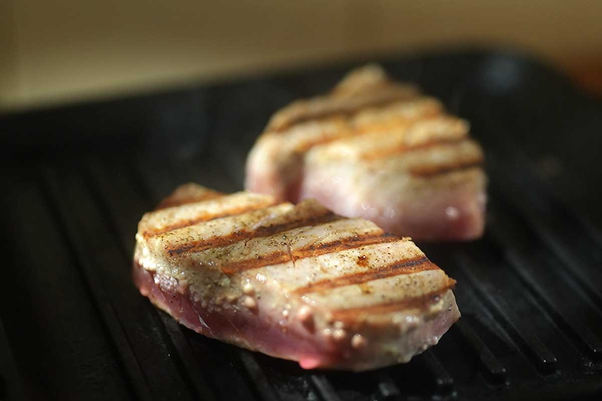 The tuna steak searing in a smoking hot cast iron pan, untouched, showing the crust forming