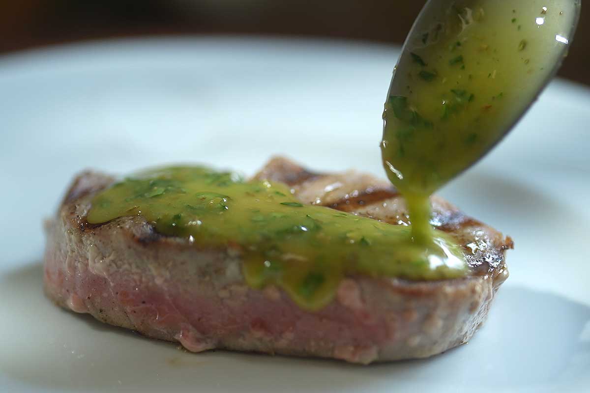 Salmoriglio being spooned generously over the rested tuna steak on a plate]