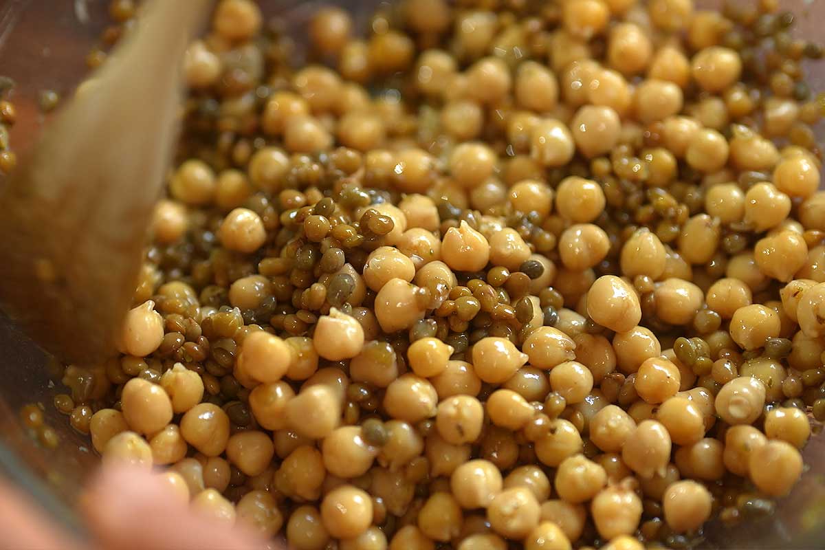 Chickpeas and lentils being tossed in lemon garlic dressing to absorb