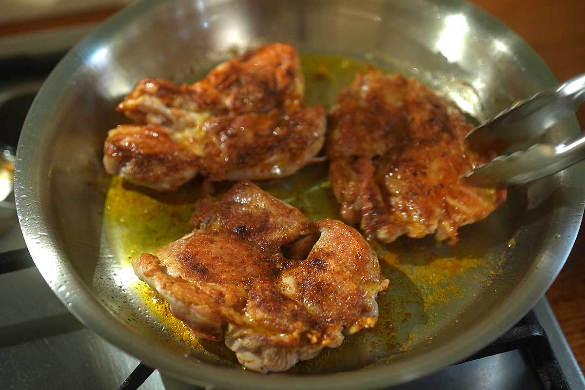 Chicken thighs searing golden in frying pan smooth side down