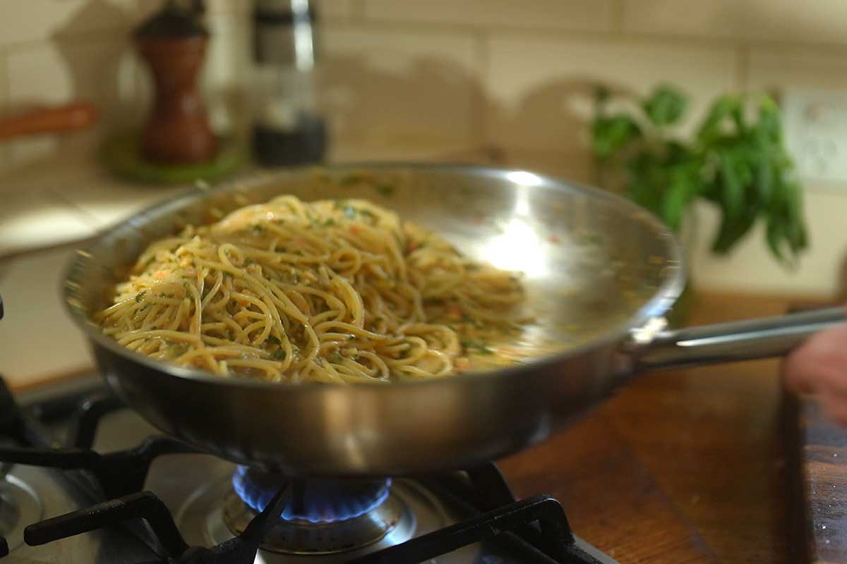 The finished pasta being tossed in the pan with the raw pesto, showing the sauce coating the spaghetti