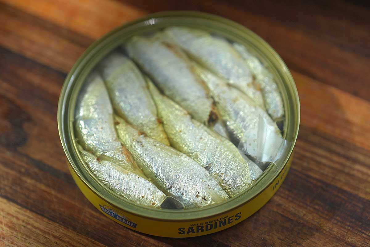 Tin of sardines opened next to lemon, chilli flakes and parsley on a chopping board