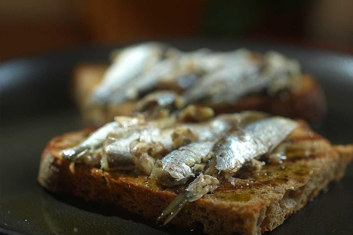 Side angle shot showing the crisp charred edge of the toast under the sardines
