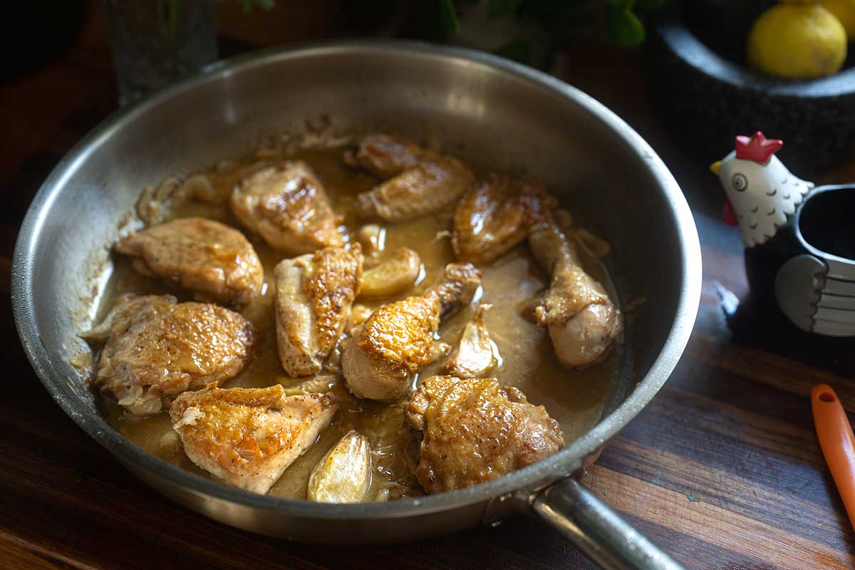 Overhead shot of the finished chicken in the pan, glossy sauce, garlic cloves and parsley scattered through]