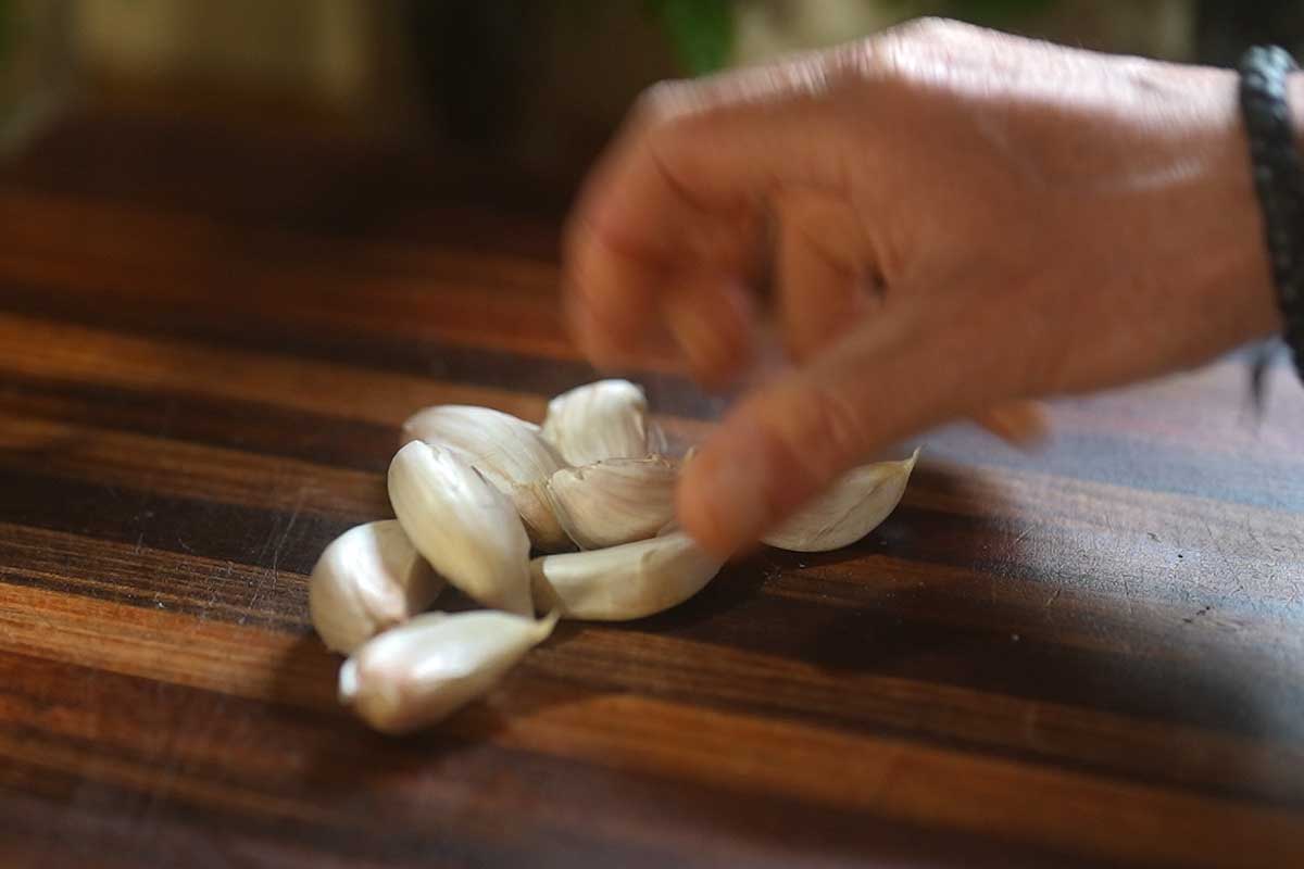 Close up of crushed garlic cloves still in their skins next to sliced garlic on a chopping board]