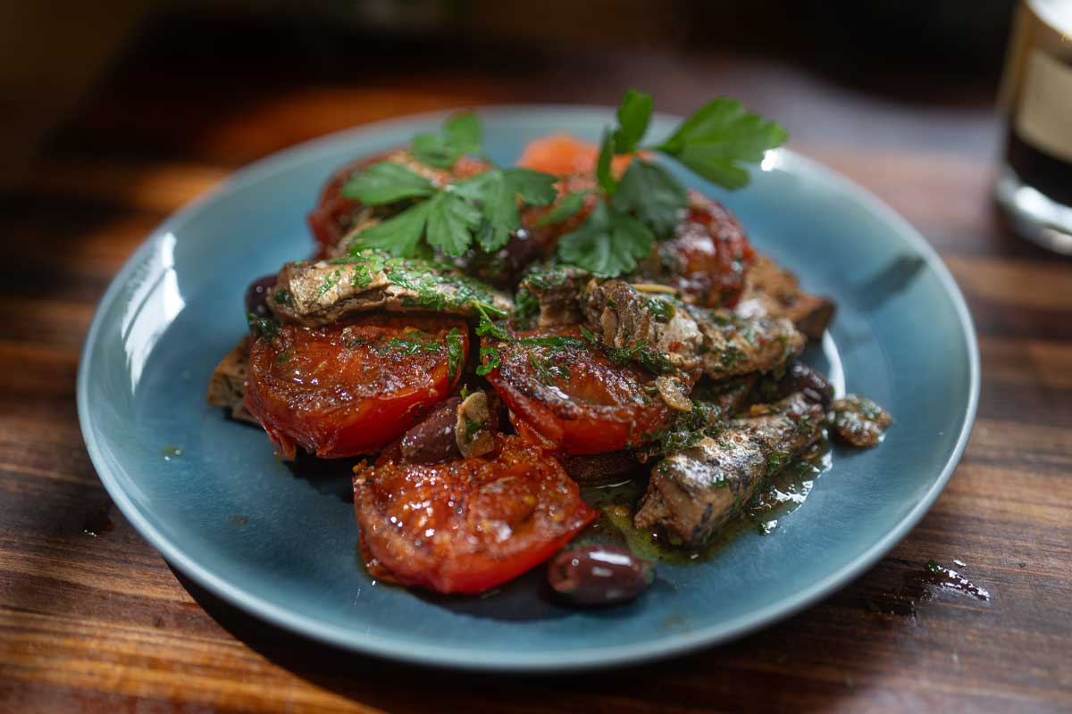 Overhead shot of the finished sardine and tomato toast on a wooden board, pan juices soaking into the bread