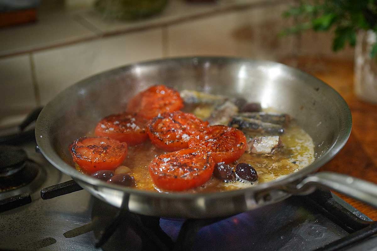 Close up of sardines in the pan with tomatoes and white wine bubbling around them