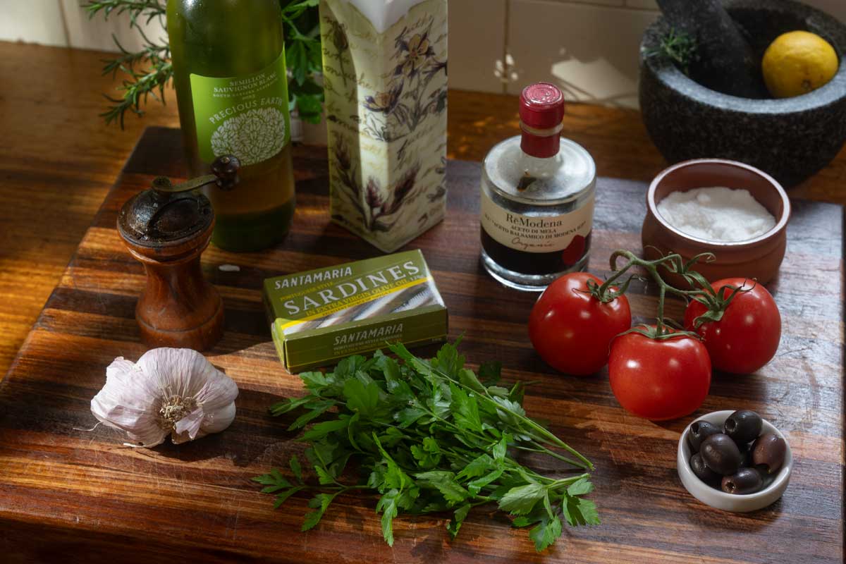 Ingredients laid out before cooking, tin of sardines opened next to ripe tomatoes and garlic]