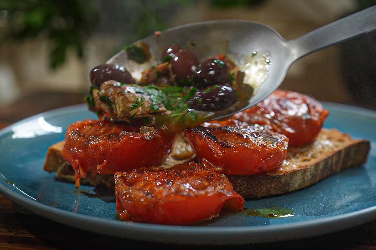 Hands spooning the warm tomato and sardine mixture over toasted sourdough