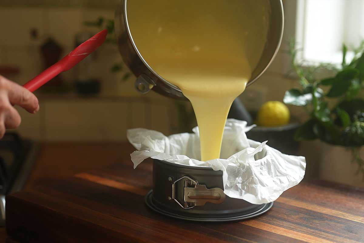 The batter being poured into the parchment-lined cake pan