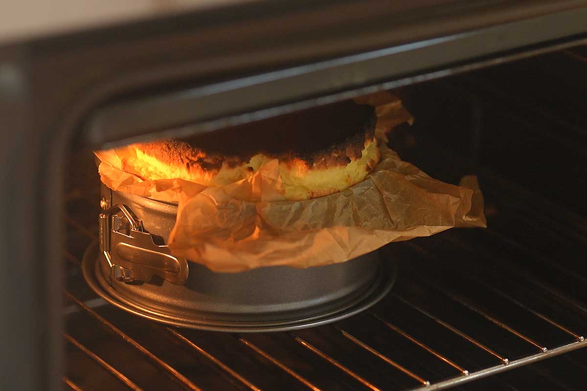 The cheesecake in the oven with the top turning deep brown