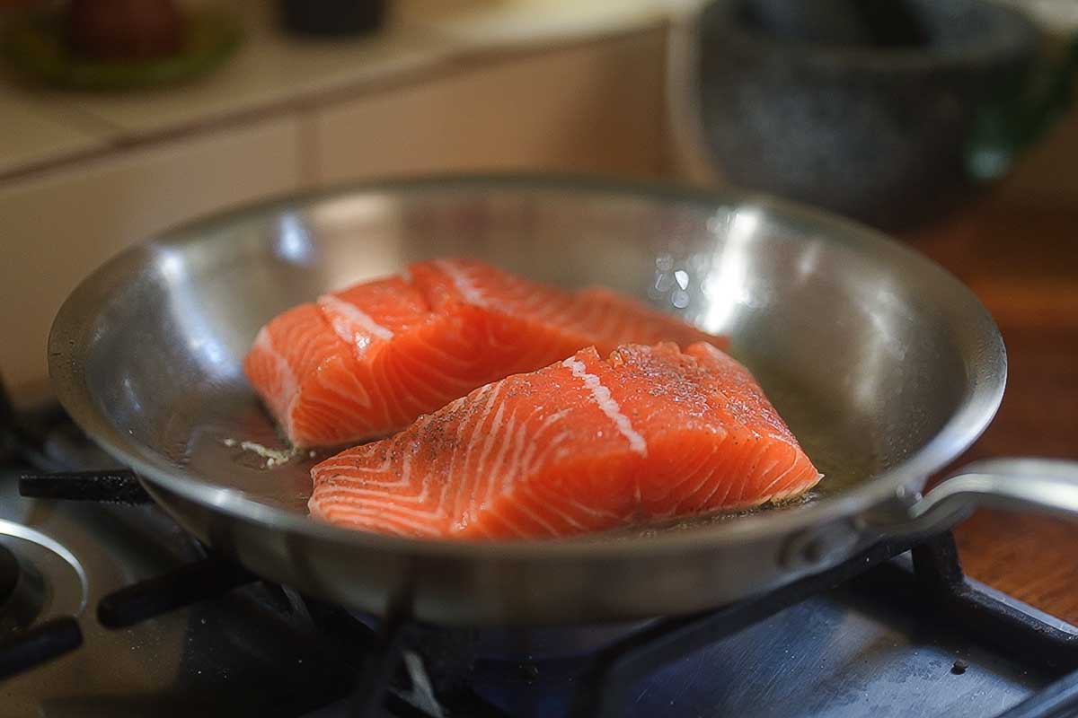 Salmon skin-side down in the frying pan, being pressed flat