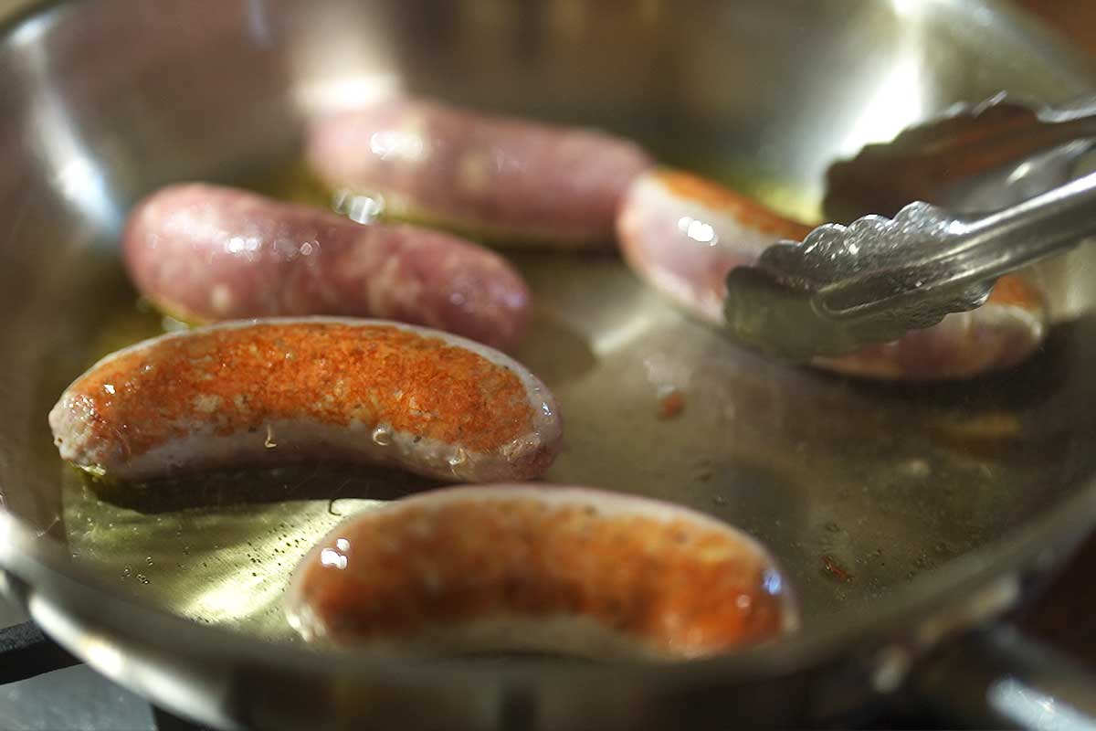 Sausages browning in a frying pan