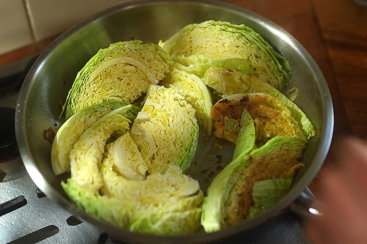 Cabbage wedges being turned in the sausage fat in the pan