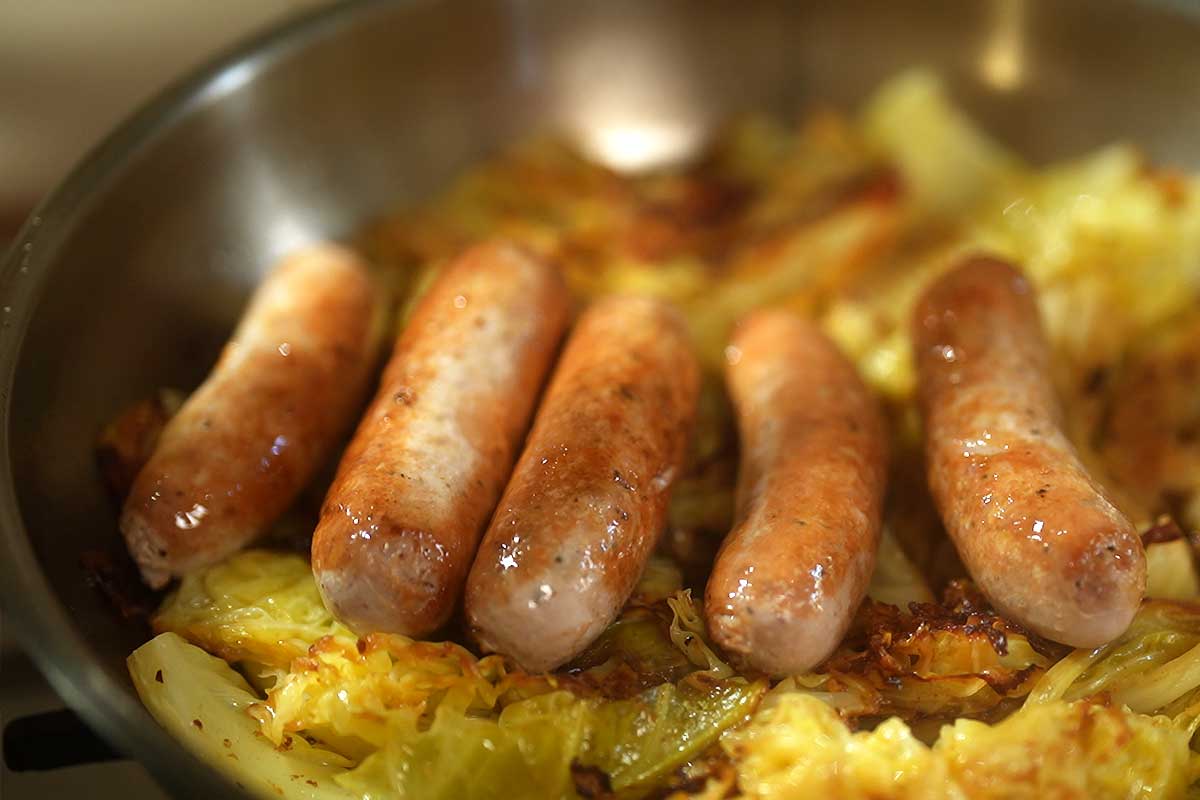 Close up of the braised cabbage and sausage in the pan, sauce glistening