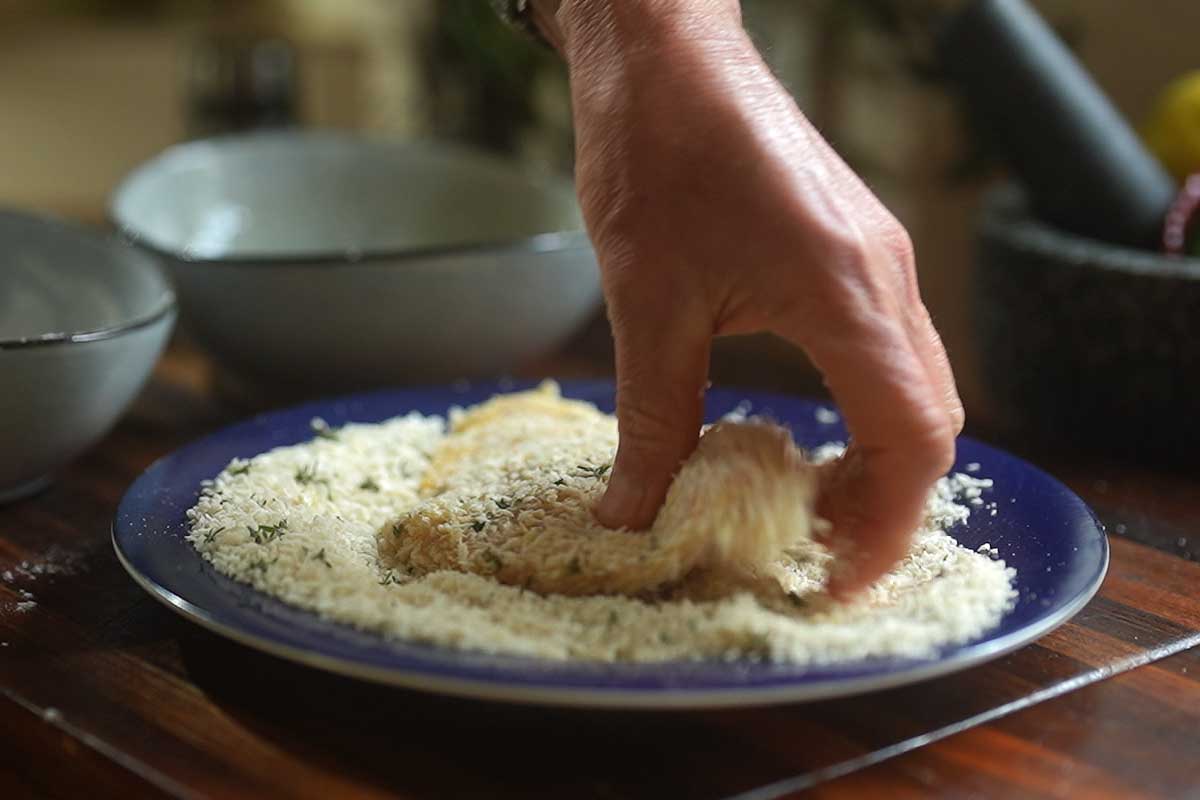 Close up of chicken cutlet being pressed into the panko crumb mixture