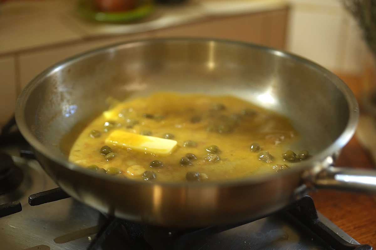 Piccata sauce being finished with cold butter swirled through, glossy and thick