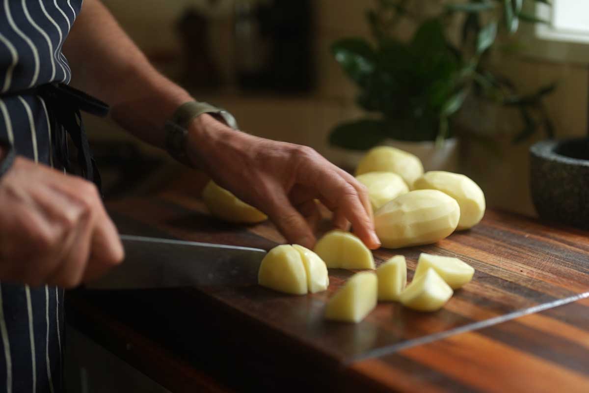 Potatoes being cut into rough, uneven chunks on a board