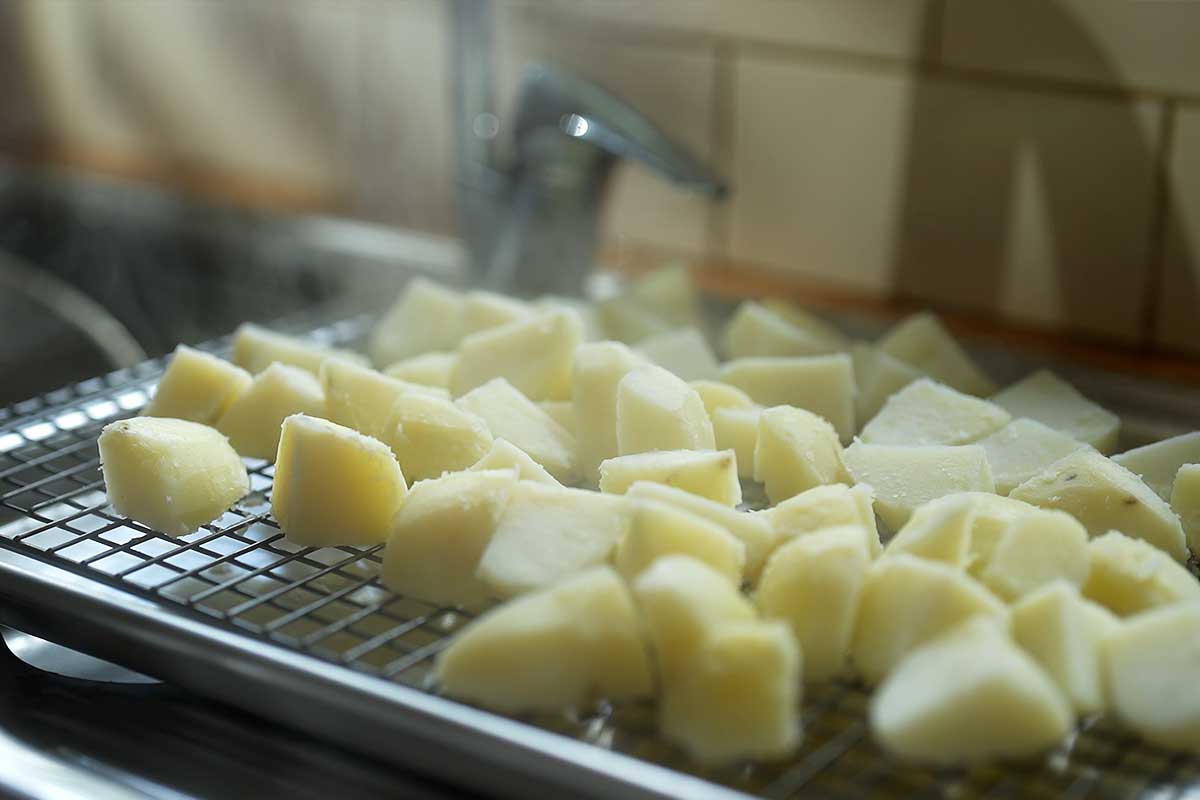 Boiled potatoes spread out on a tray, steam rising as they dry
