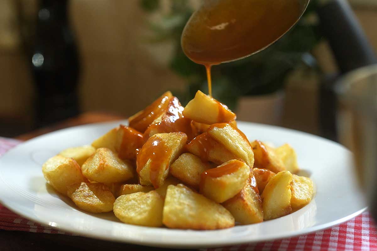 Warm brava sauce being spooned generously over crispy fried potatoes