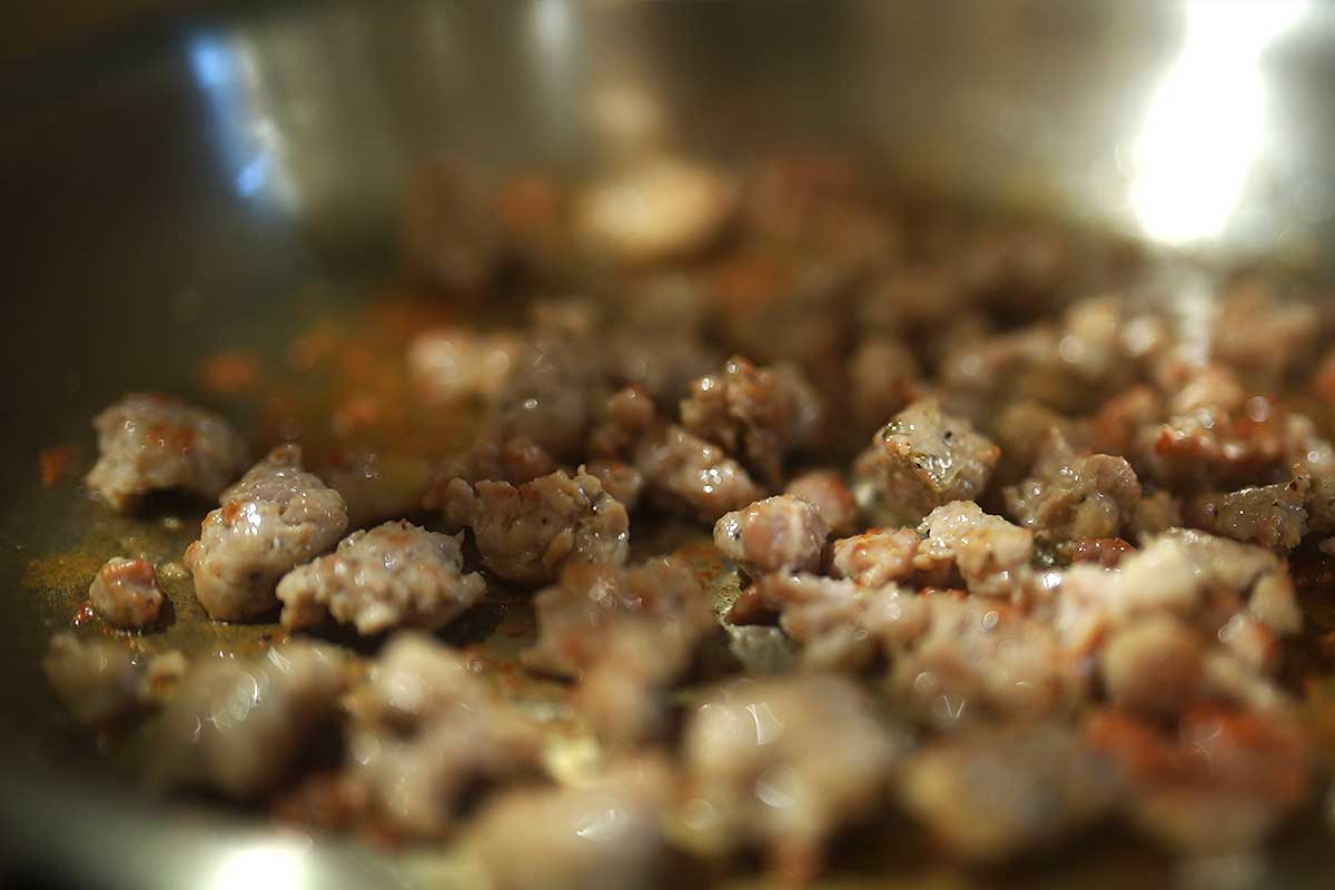 Sausage chunks browning in the frying pan, golden edges forming]