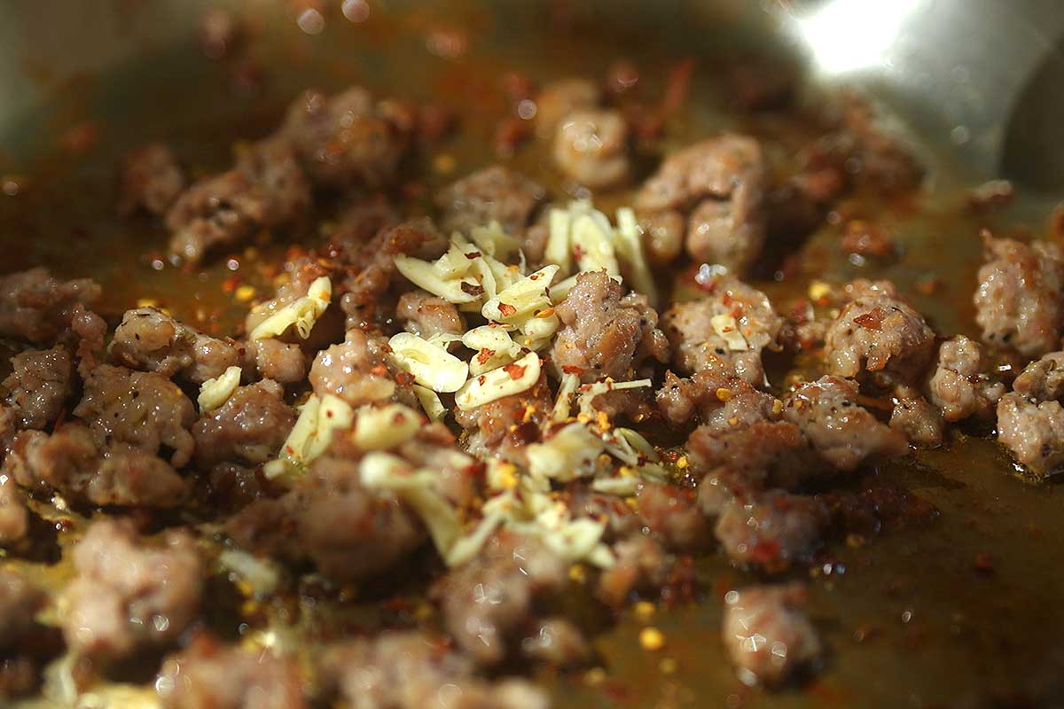 Sliced garlic and chilli flakes sizzling in the sausage fat