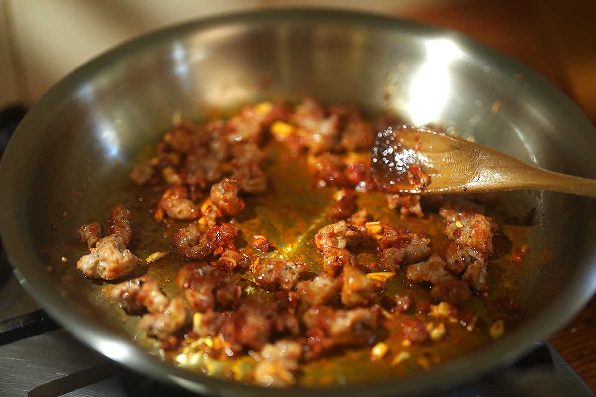 Tomato paste being stirred in the frying pan, darkening and starting to caramelise
