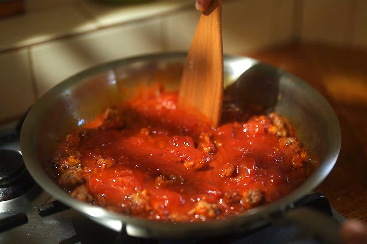 The crushed tomatoes simmering and reducing in the frying pan