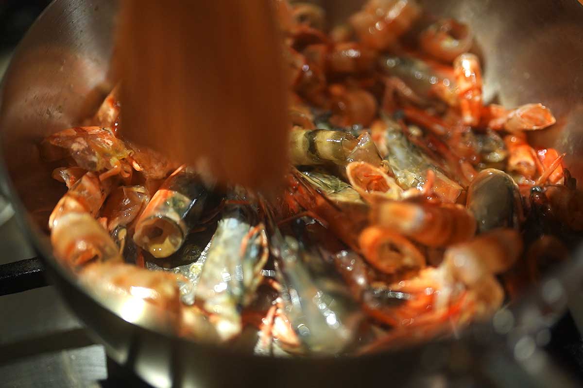 Crushing shrimp heads with a wooden spoon in the pan