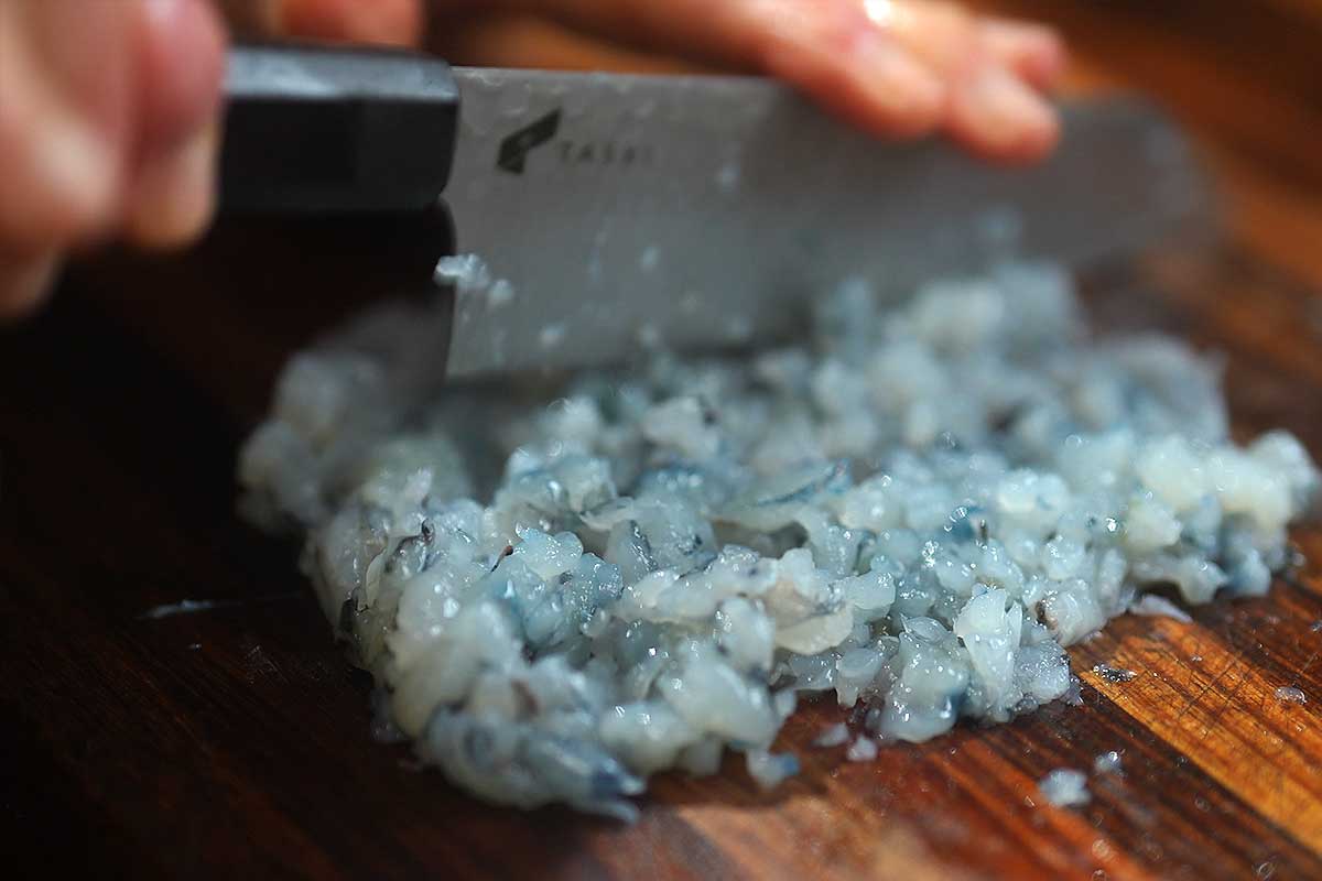 Shrimp being finely chopped on a board into a coarse mince