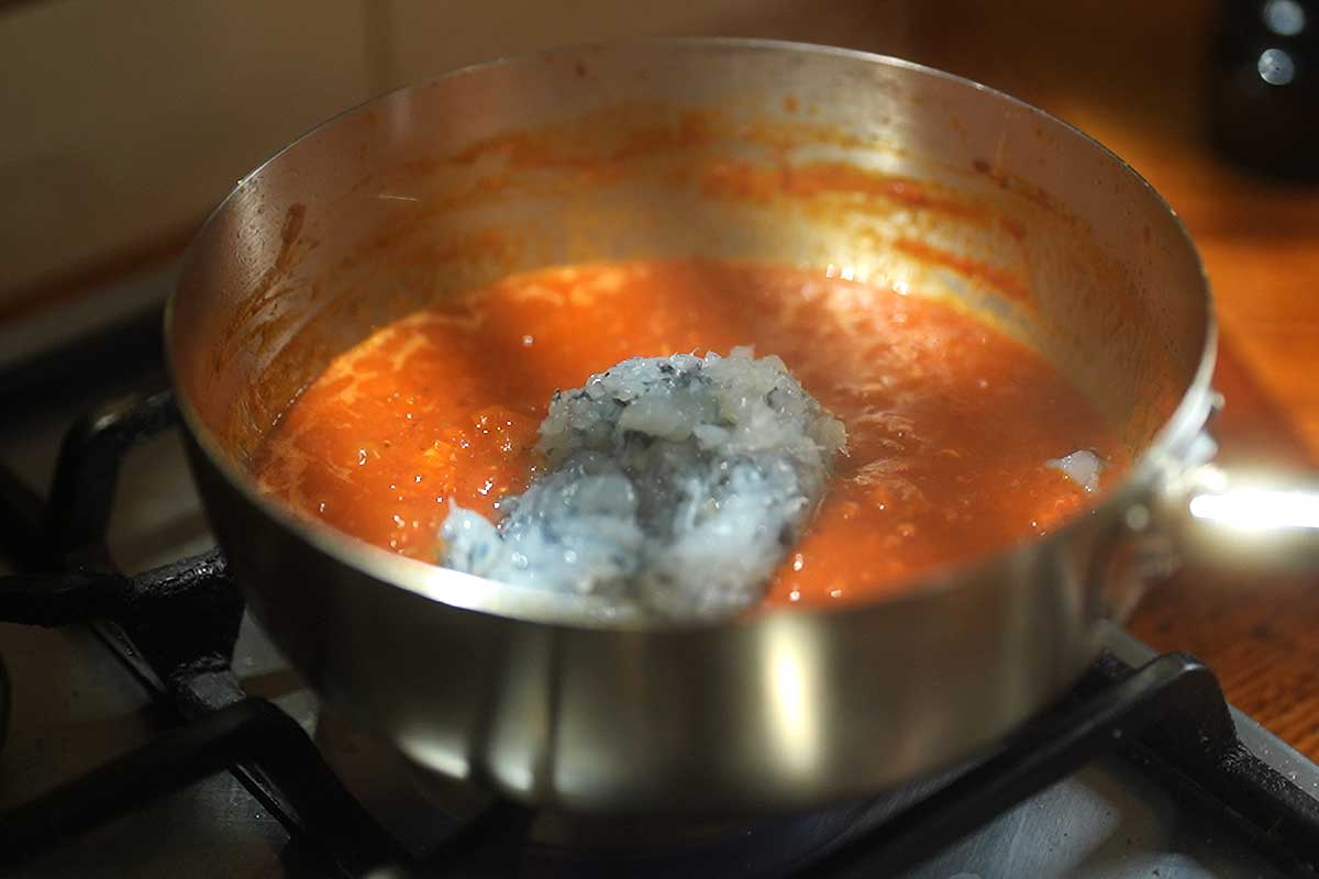 Shrimp pieces turning pink and opaque as they're stirred through the sauce