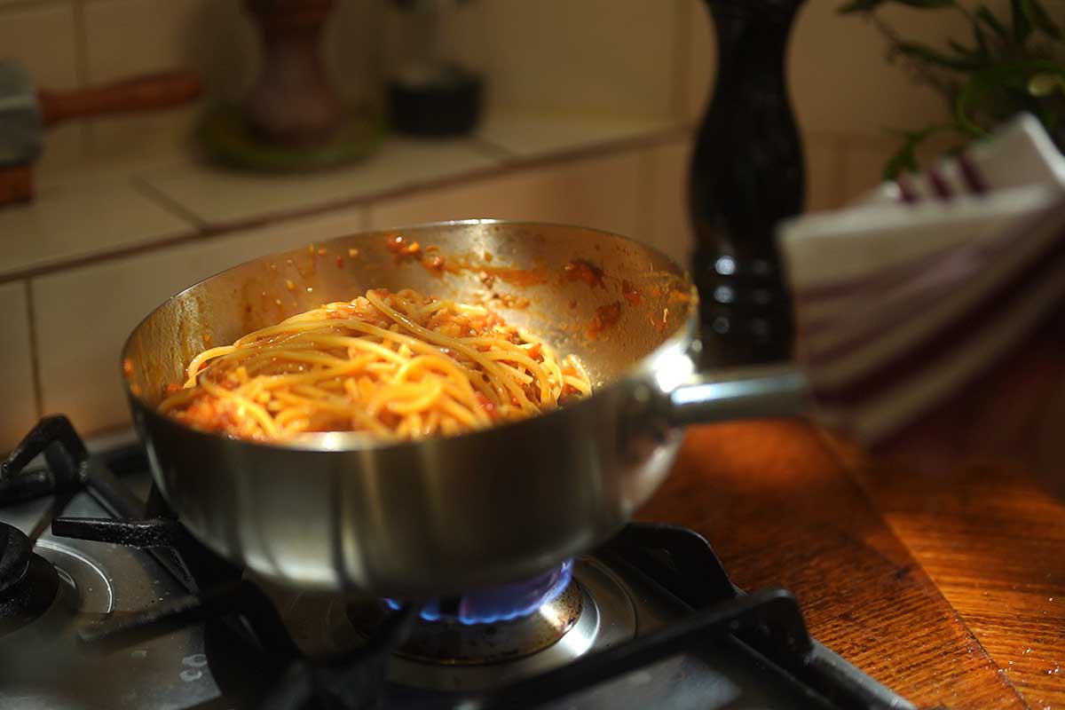 Spaghetti being tossed through the sauce in the pan]