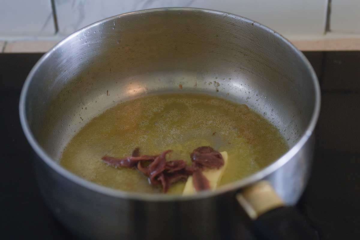 Anchovy fillets going into the melted butter in the frying pan