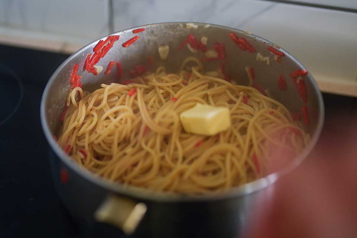 Cold butter pieces being added to the spaghetti in the pan]