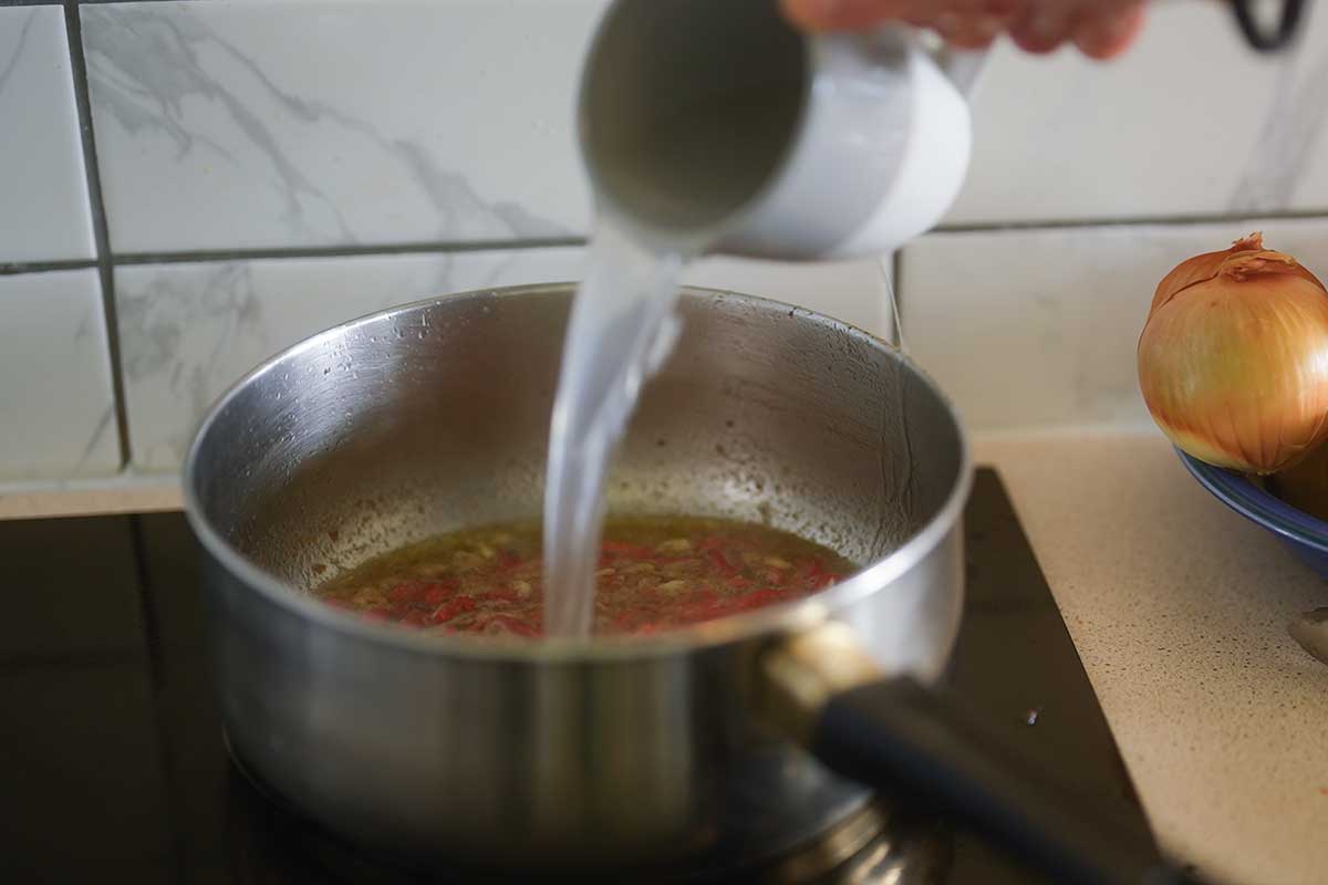 Hot pasta water being poured into the anchovy butter and simmering