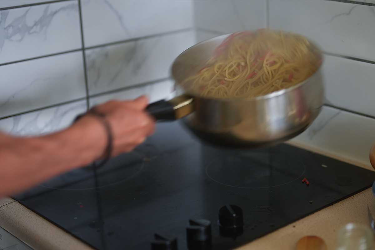 Spaghetti being tossed vigorously in the pan as the sauce thickens