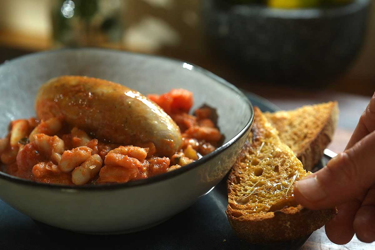 Fagioli all'Uccelletto served in bowl with grilled garlic bread alongside