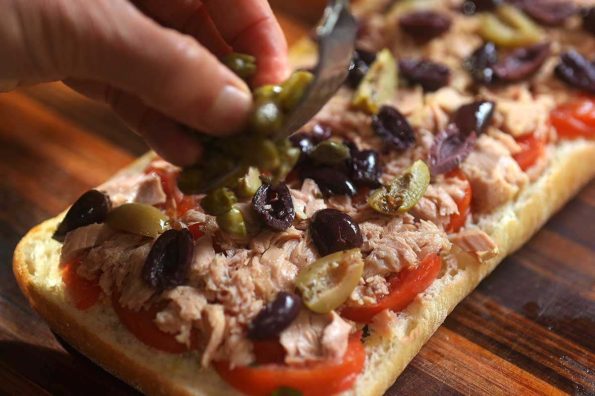 Layers of tuna olives capers and pickled onion being built on bread