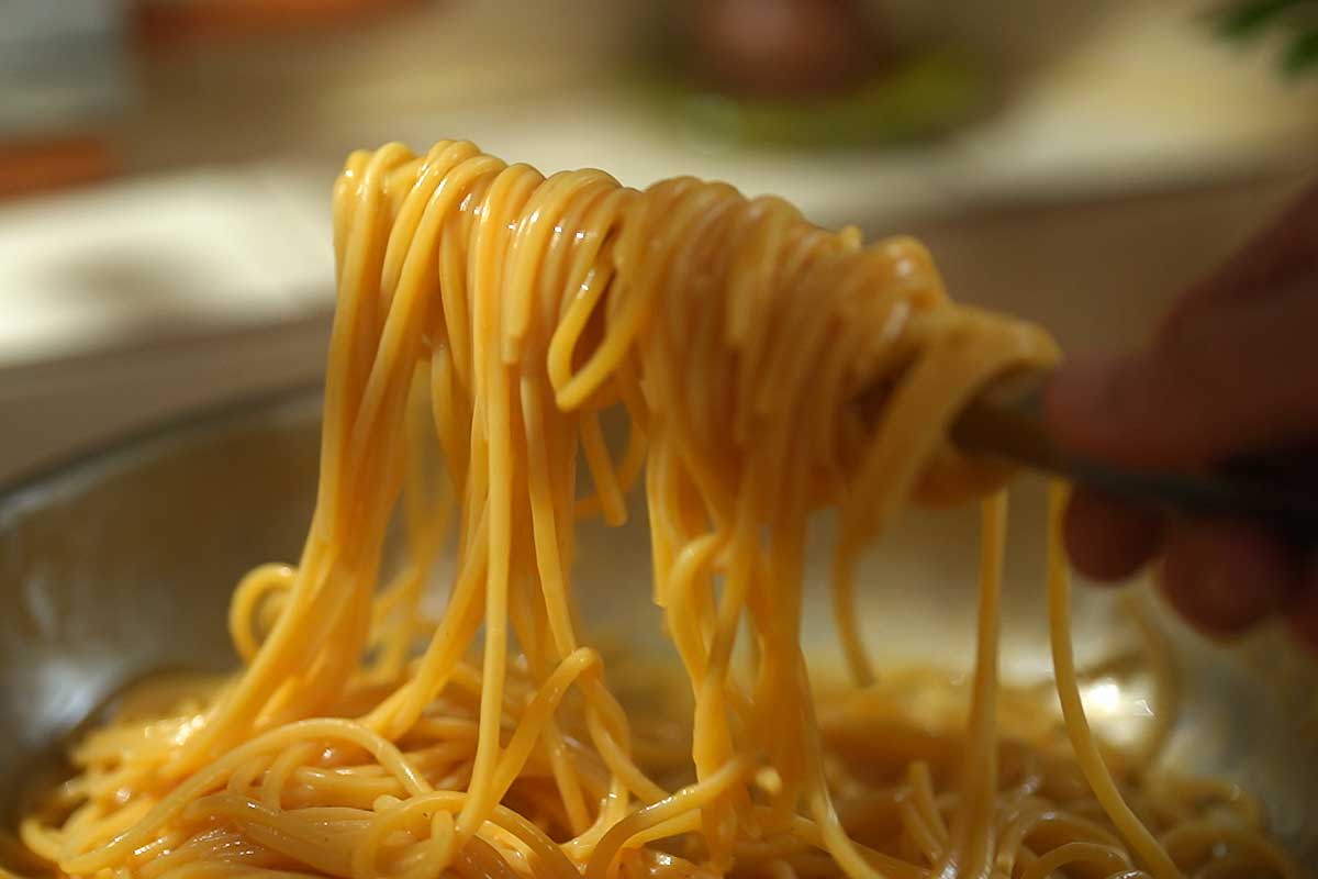 Close up of silky glossy spaghetti coated in emulsified tomato olive oil sauce